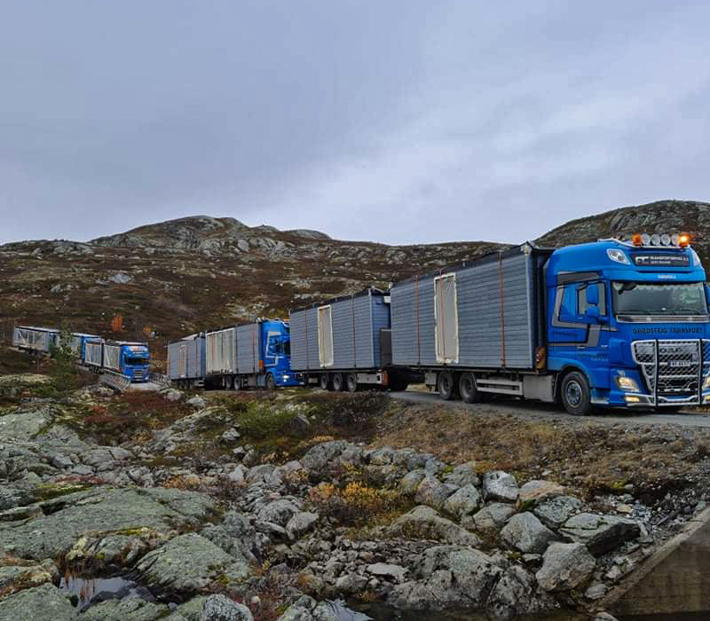 Blå lastebiler frakter brakkemoduler over fjellet